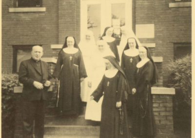 Priest and nuns on steps of Riverside in sepia